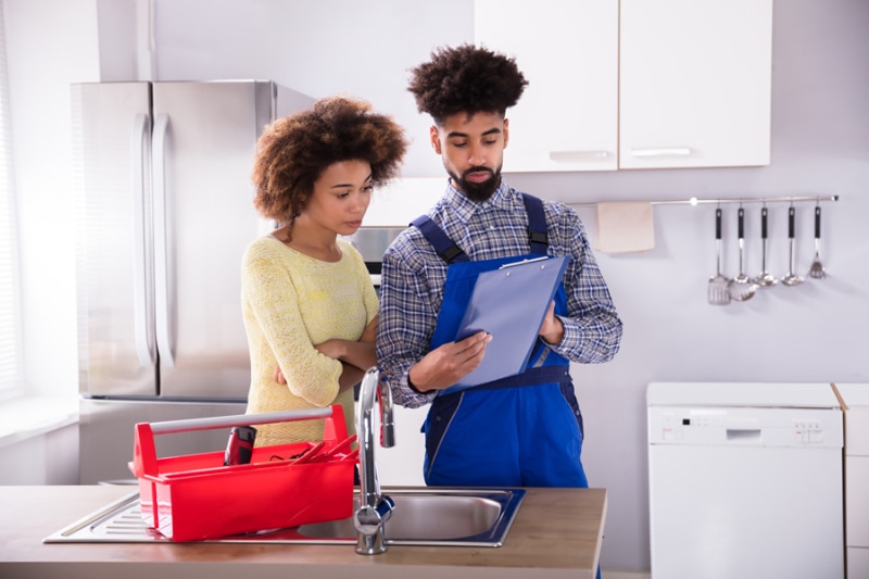 Troubleshooting Air Conditioning Problems Before Calling the Pros - Young Male Plumber Looking At Woman Signing Invoice In Kitchen