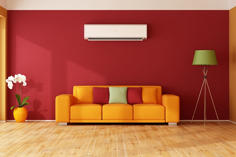 Advantages of Installing a Ductless System. Red and orange living room with colorful sofa and air conditioner.