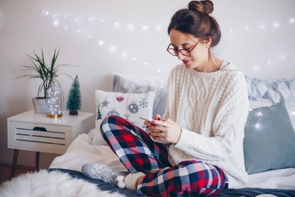 Have Your Furnace Repaired This Winter! Image shows woman sitting on her bed and looking at her phone.